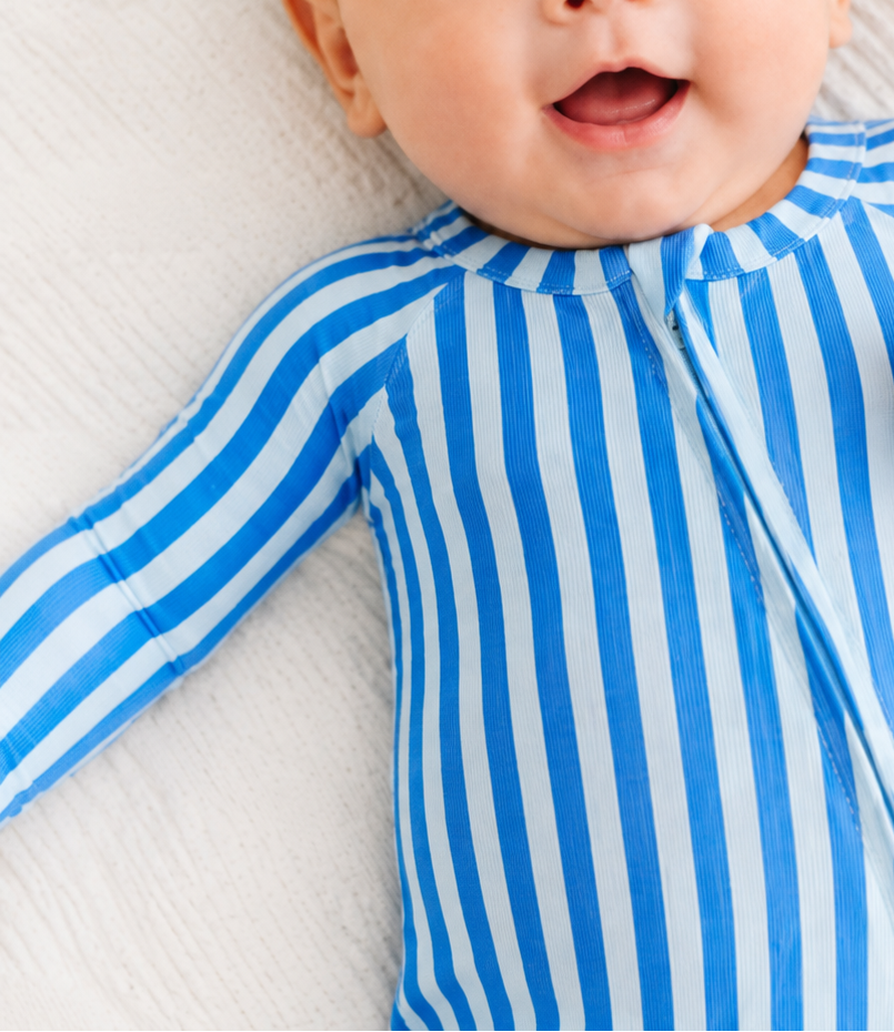 Baby wearing a blue striped onesie on a white blanket